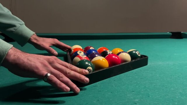 Pool player slides a triangle rack filled with billiard balls away from the cushion, positions the balls for the opening break and removes hands from the table, close-up preparation, horizontal video