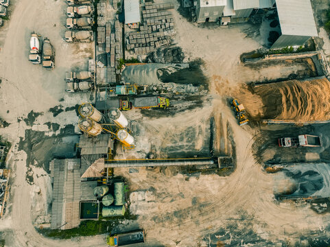 Aerial view of a cement plant featuring concrete silos, cement mixer trucks, stockpiles of raw materials, and heavy machinery in an industrial setting, Klapanunggal, West Java, Indonesia.