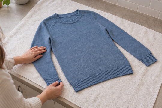 Hands shaping a blue sweater flat on a towel