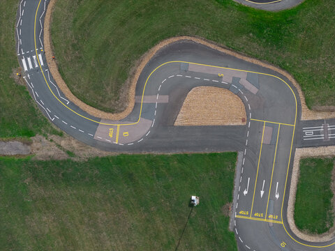 Aerial view of a vehicle testing track with road markings, stop signs, and directional arrows surrounded by green grass United Kingdom.
