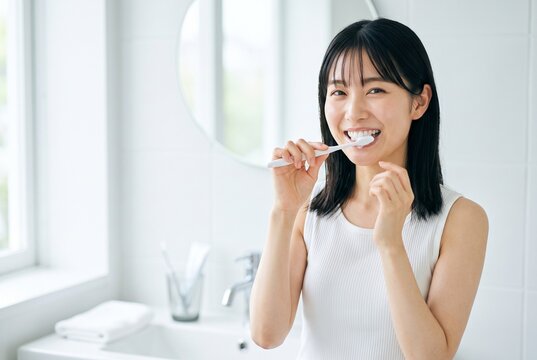 朝の洗面台で歯ブラシを使い口腔ケアをする若い女性、歯科・ヘルスケア広告向け