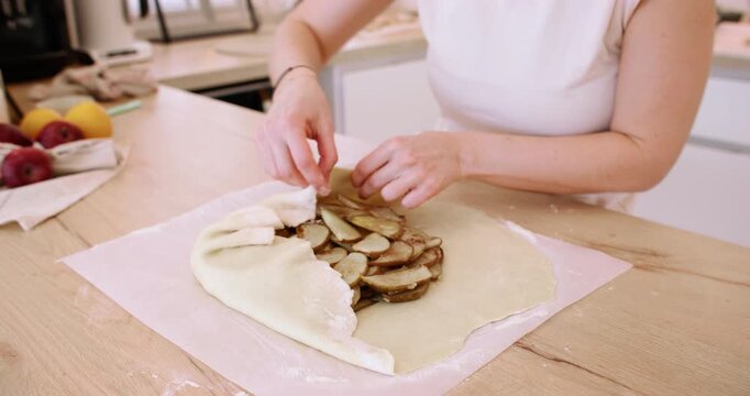 Fruit pastry. Cooking galette. Female baker hand covering sliced pear pie with flattered dough flour sheet on home kitchen paper parchment.