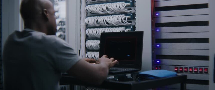 Male Monitoring Server Status, Performance Analytics at Computer Workstation When Critical Alert Interrupts Dashboard. Server Room Operations, Technical Troubleshooting, System Reliability Management.