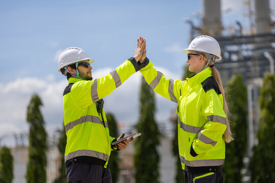 Industrial engineers giving high five celebrating successful inspection at plant, Chemical plant inspectors giving high five after finishing project inspection outside refinery