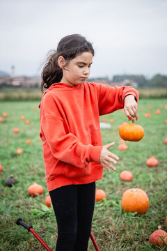 Girl holding a small pumpkin by its stem in an autumn pumpkin patch