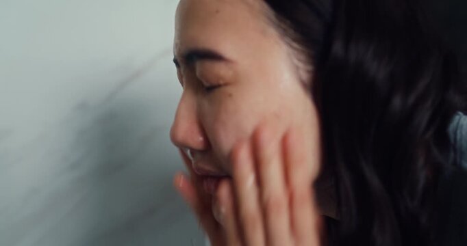 Young Asian woman washes face with cleansing foam in bathroom mirror at home. Daily skincare beauty facial routine, Healthy fresh moisture cosmetic lotion, Personal hygiene wellness care concept.