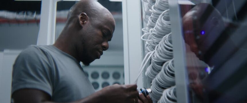 Male System Administrator Checks Server Rack Patch Panel and Network Switches inside Modern Server Room. Experienced IT Technician Performs Hardware Audit and Infrastructure Troubleshooting.