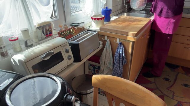 Woman cleans an empty glass bowl over the kitchen sink after preparing food. A closed air fryer remains on the table in the background while she tidies the kitchen and cleans up. Static shot.