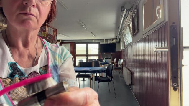 Close-up of a woman carefully brushing and cleaning a removed door lock cylinder while the key remains inserted. The open door and hands-on maintenance process show practical home repair. Static shot.