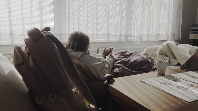 Unwell young woman rests at home while texting school friends on her smartphone, maintaining social contact despite being physically unable to attend school.
