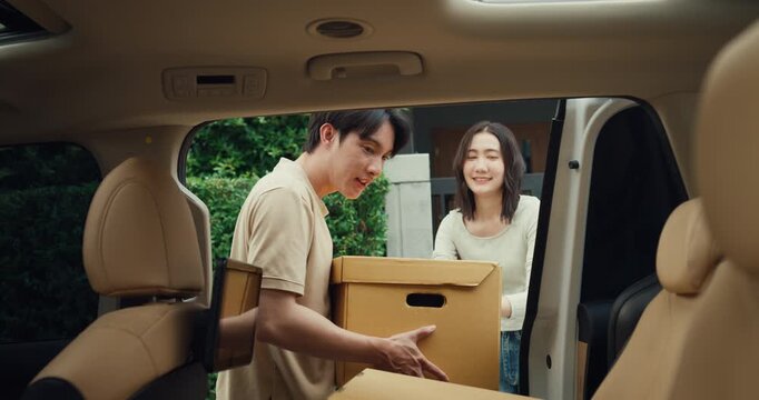 Young Asian couple carries cardboard boxes to load car trunk while moving out. Family relocation home mortgage loan, Real estate moving transport vehicle, New house package delivery pack concept.