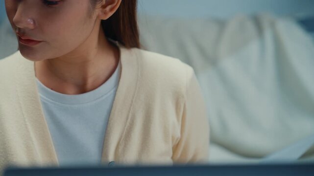 Close up young Asian woman reviews financial documents, bills and expenses on laptop at home. Personal finance budget planning, Tax invoice paperwork review, Household savings and expense management.