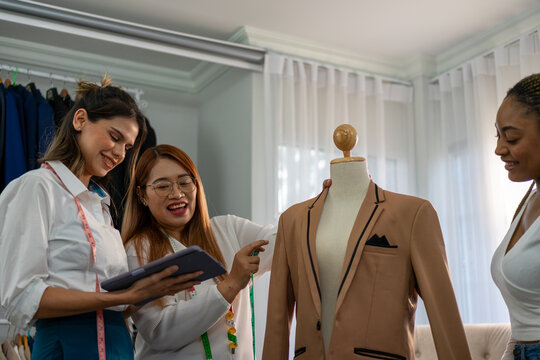 Women laughing while reviewing tablet near blazer mannequin