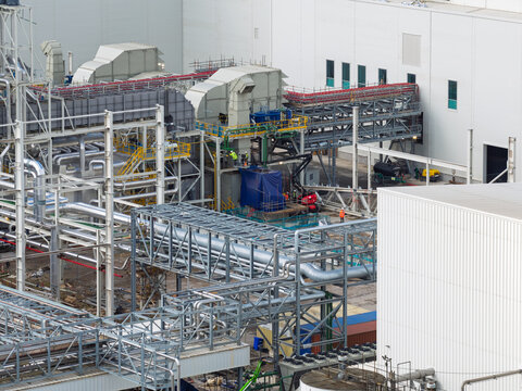Aerial view of a paper mill industrial facility featuring complex metal piping, large ventilation units, structural steel framework, and workers in high-visibility gear on site in the United Kingdom.