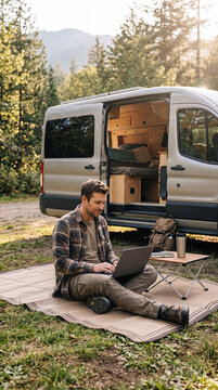 Man Working on Laptop Outside Camper Van During Road Tri