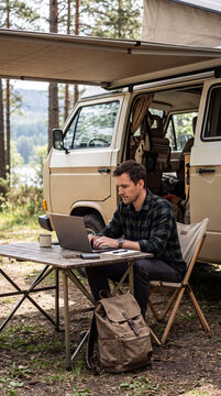 Man Working on Laptop Outside Camper Van During Road Tri