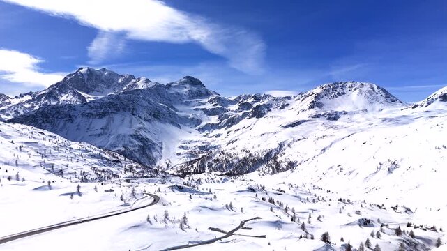 Vehicles on road on Simplon Pass with Mount Fletschhorn covered in snow. Aerial