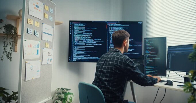 Young Caucasian male programmer writes code using multiple screens in home office workspace. AI development, cybersecurity, network database system, software engineering, remote tech startup concept.