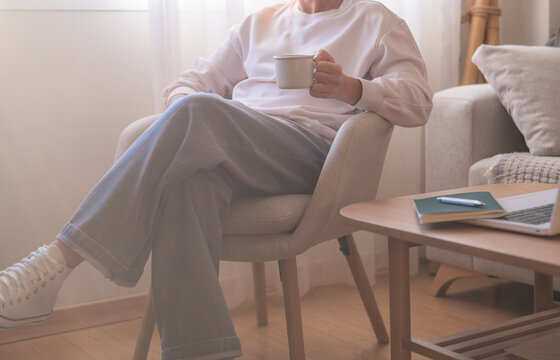Person relaxing in a sunlit living room, sipping coffee beside an open laptop and notebook, embracing a slower morning and a moment of mindful disconnection