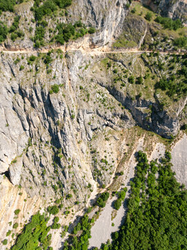 Aerial view of the rugged limestone cliffs and rocky slopes of Durmitor, with a narrow road carved into the rock face and green forests below in Zabljak, Zabljak Municipality, Montenegro.