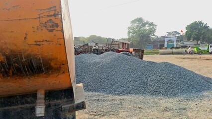 Large pile of crushed gravel stones at a construction site with heavy machinery and a dumper truck in the foreground © Zahoor