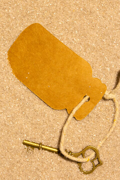 Old vintage brass key partly covered in sand with a blank card label tag background backdrop.