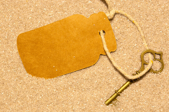 Old vintage brass key partly covered in sand with a blank card label tag background backdrop.