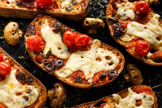 Halloween bruschetta toasts with ghost shaped melted cheese, cherry tomatoes, black olives and spooky mushrooms, close-up