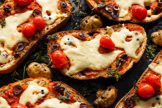 Halloween bruschetta toasts with ghost shaped melted cheese, cherry tomatoes, black olives and spooky mushrooms, close-up