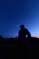 Silhouette of a person in nature observing night sky, Moon, stars and planets from a remote location. © astrosystem