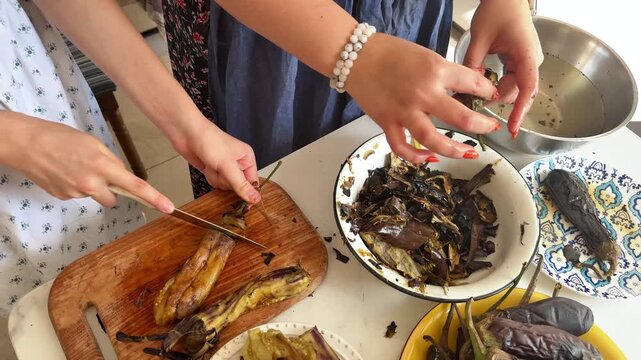 Women peel roasted eggplants with water, homemade vegetable preparation