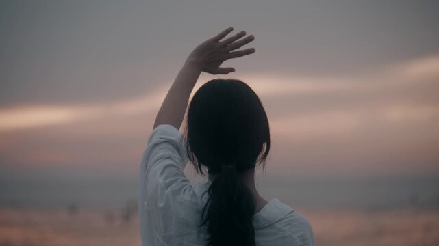 Rear View of Woman Standing on Beach and Shielding Eyes looking at Ocean during Sunset