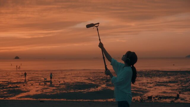 Woman Holding Shotgun Microphone on Boom Pole to Record Nature Sound on Beach at Sunset