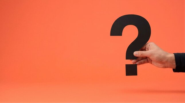 Hand holding black paper question mark on coral orange background. Large copy space for questions and answers layout. Curiosity, doubt and FAQ concept. Decision making and problem solving