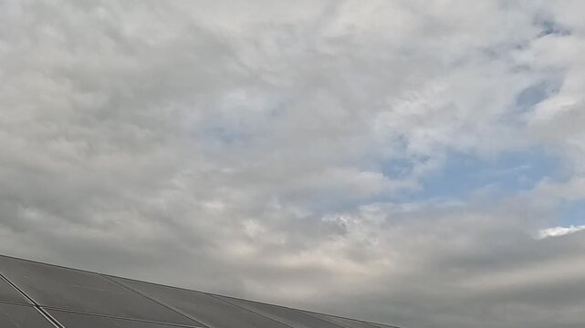 Bottom edge of solar panels looking up at cloudy sky with blue patch