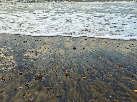 Gentle ocean waves wash over a wet sandy beach scattered with small pebbles and stones.