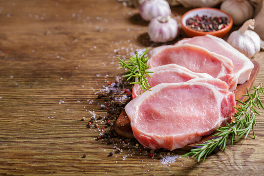 fresh pork chops with rosemary and spices on wooden table