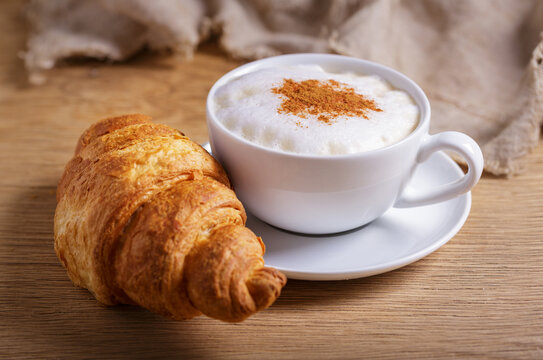Cup of cappuccino coffee with croissant on wooden table