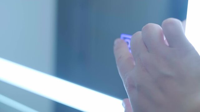 Female finger pressing touch button to turn on smart LED mirror. Close up of activating light on modern bathroom vanity. Smart home technology and electric illumination.