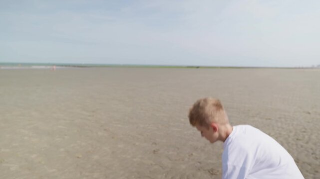 Boy walking across a wide sandy beach on a sunny day slow motion 8 years old child alone by the sea