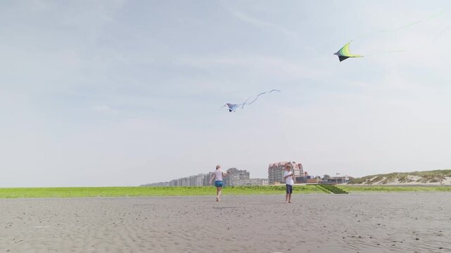 Boy and girl flying colorful kites on a sandy beach near dunes slow motion children on the seashore