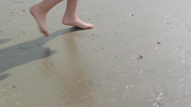 The boy's feet are walking on wet sand unrecognizable child on the seashore