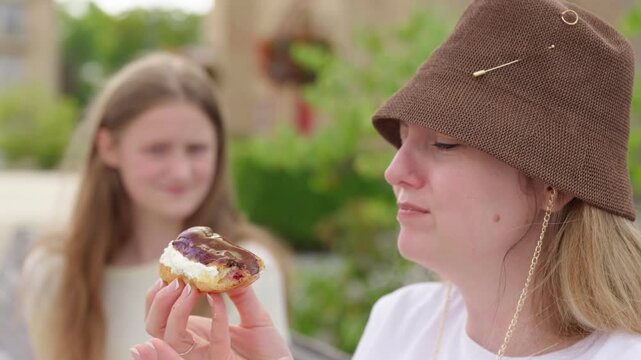 Mother offering a cream filled pastry to her daughter sitting on a park bench the girl refuses to eat sweets close-up