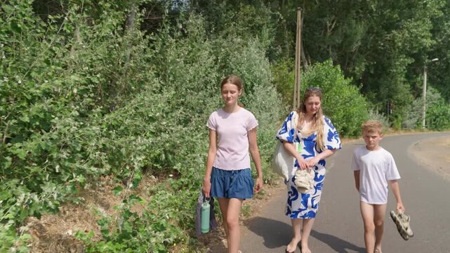 Woman and two children walking along a tree lined road slow motion a family walk barefoot