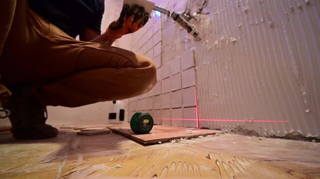 Tiler installing ceramic wall tiles in a bathroom using a laser level for precision