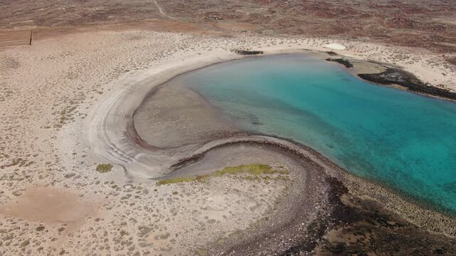 Close aerial of the curling sand and lava shoreline of La Concha lagoon at low tide, forming a natural spiral of turquoise water, Isla de Lobos, Fuerteventura.