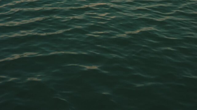 Close-up shot of Lake Peten Itza water, capturing soft ripples and rich textures. Natural sunlight enhances deep blues and greens with subtle reflections, conveying calm mood.