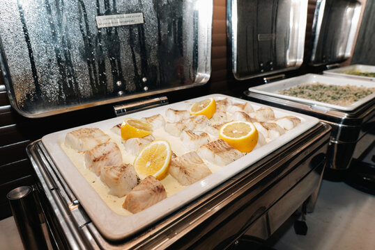 Baked white fish fillets with lemon slices in a buffet chafing dish