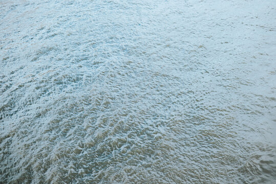 Foam and ripples move across a water surface, forming overlapping patterns. The frame contains water only, with no visible shoreline, people, or objects