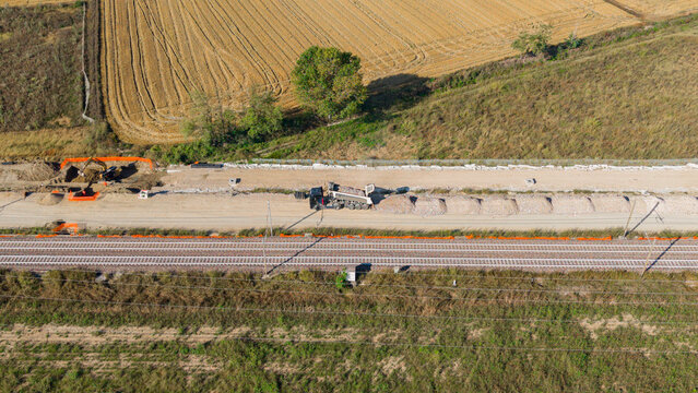 Aerial view of construction of a new railway line with heavy machinery and gravel piles alongside existing tracks in Milan, Lombardy, Italy.